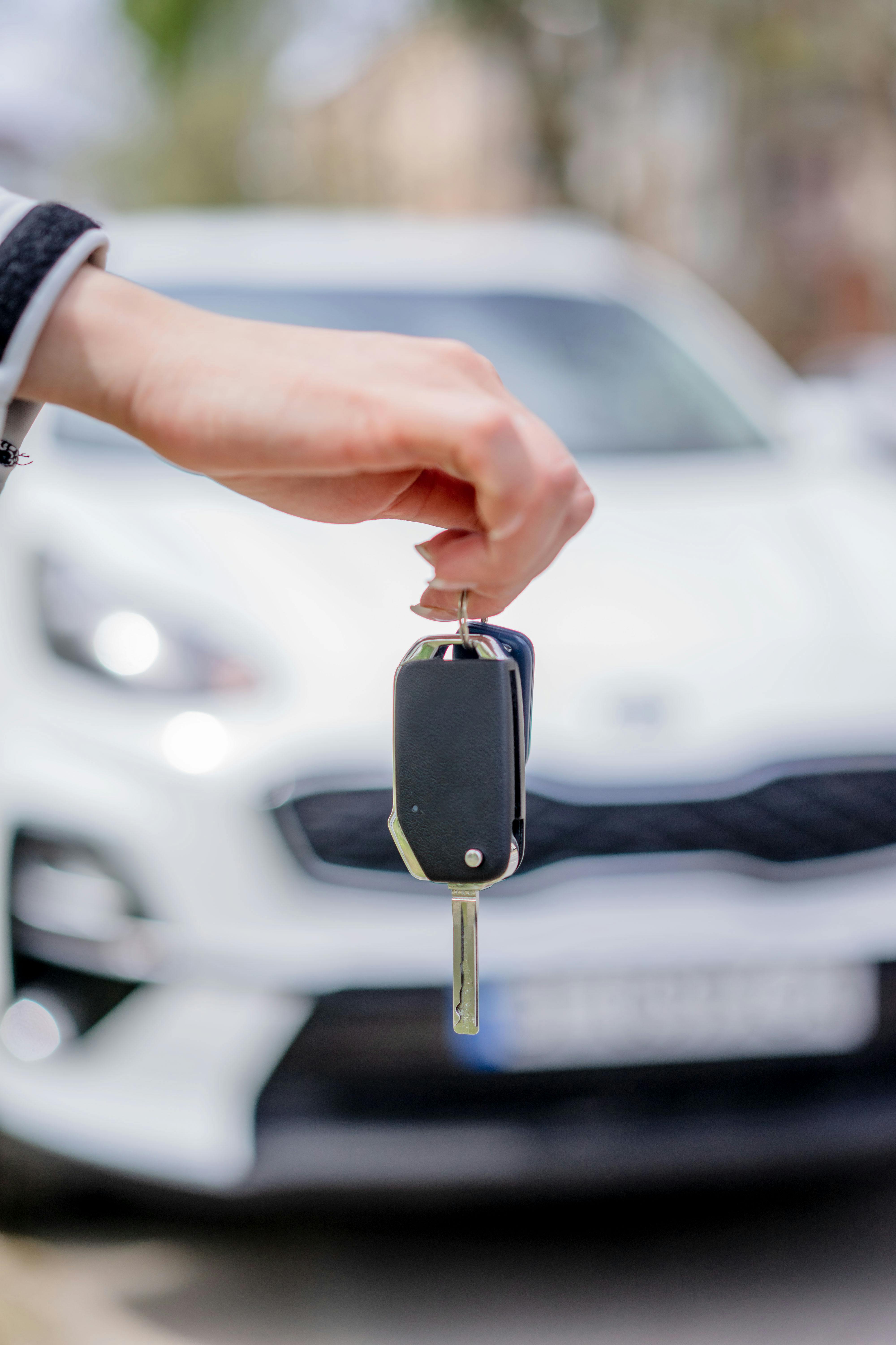 Close-up of a hand holding a car key, with a white car in the background outdoors.